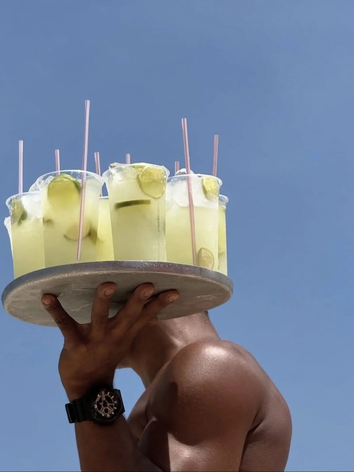 A tray of caipirinhas held aloft against a blue sky